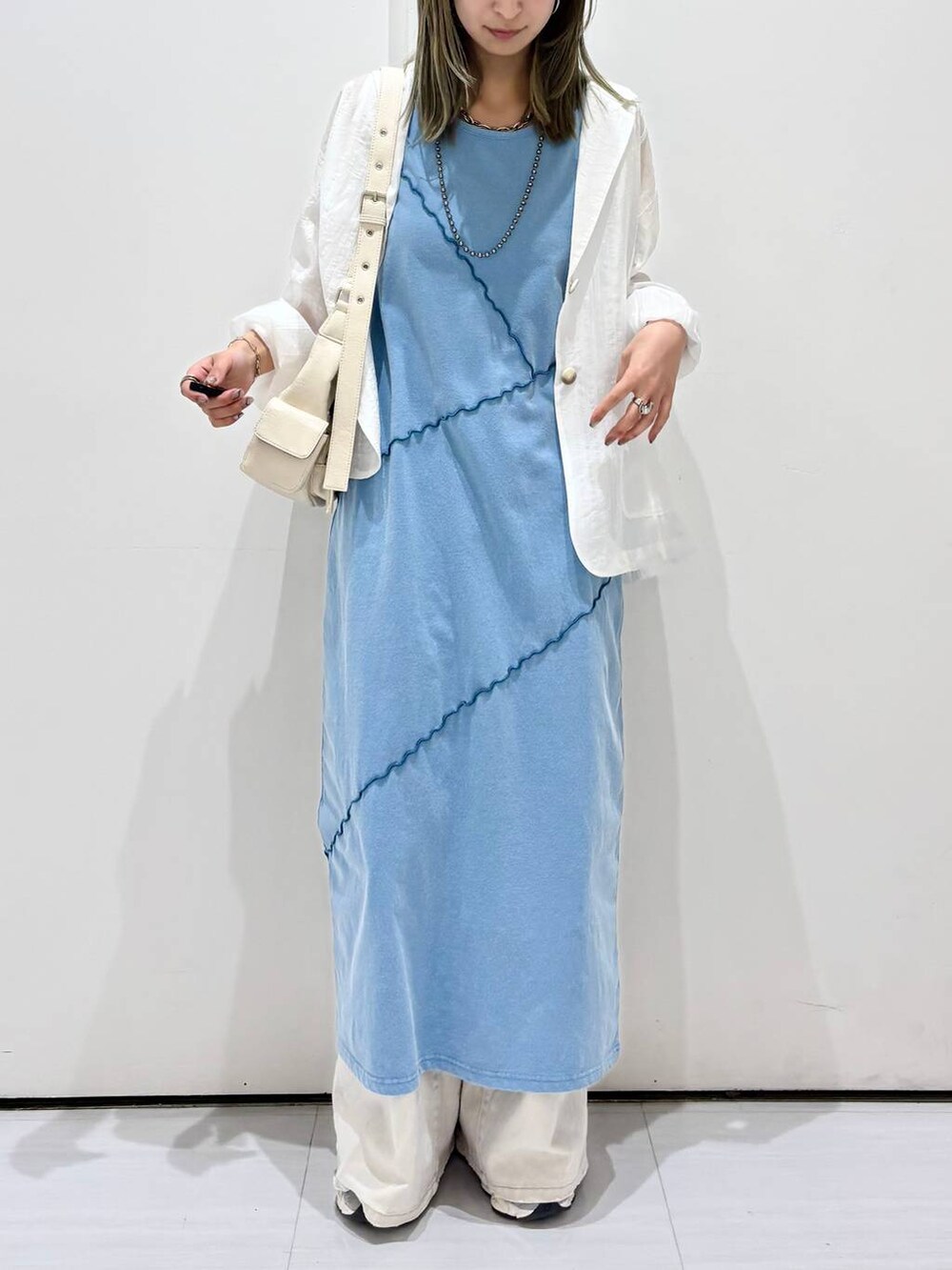 グレー系のデニムパンツ、ホワイト系のテーラードジャケット、ブルー系のワンピースを着用したレディースの春コーディネートの2枚目の写真