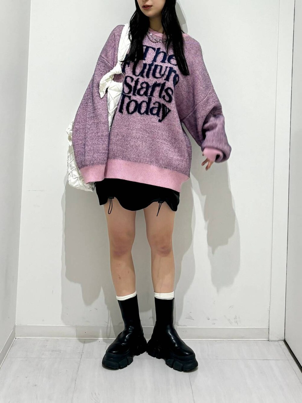 ブラック系のブーツ、ピンク系のニット/セーター、ホワイト系のショルダーバッグを着用したレディースの冬コーディネートの2枚目の写真