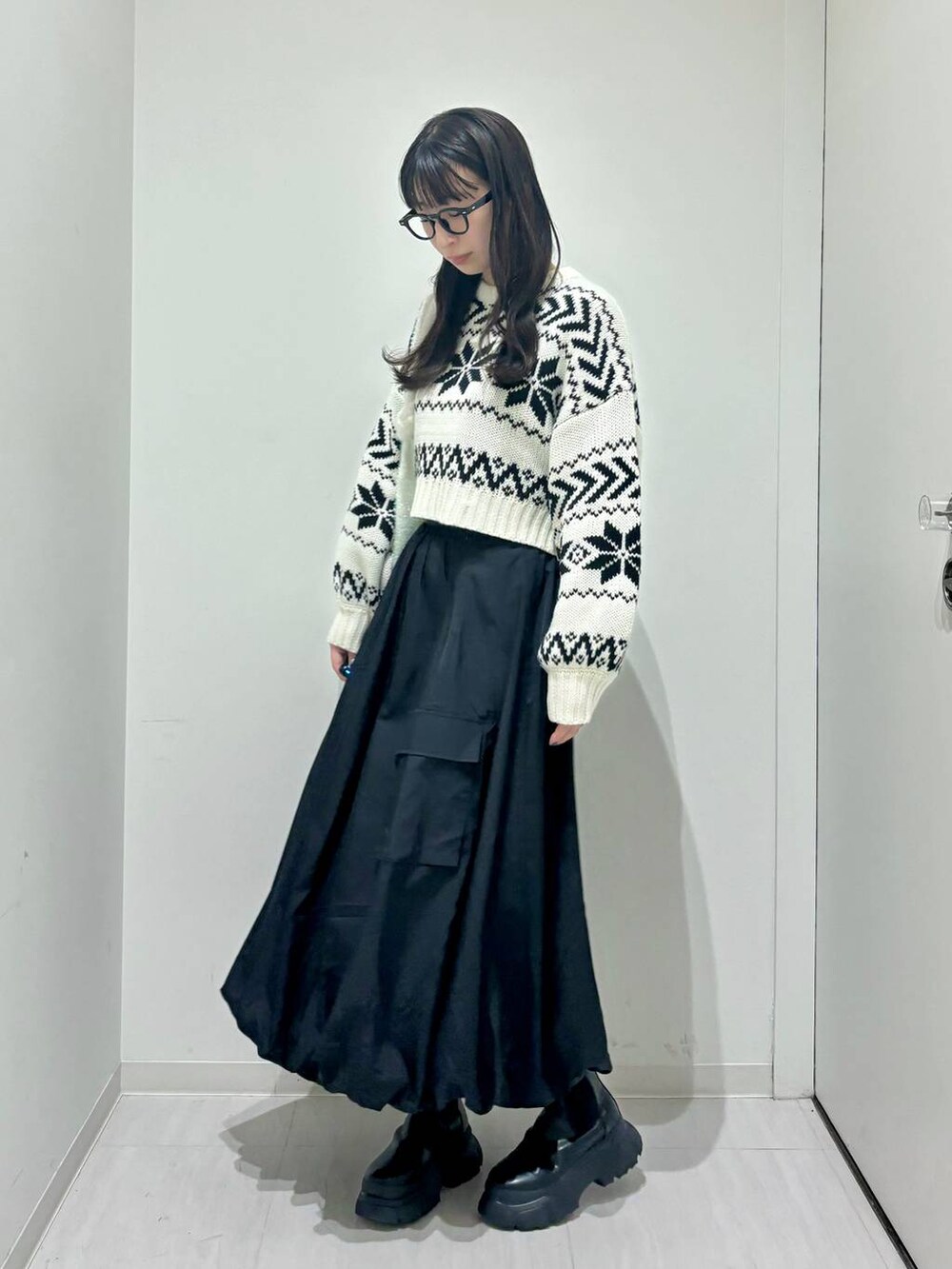 ブラック系のブーツ、ホワイト系のニット/セーター、ブラック系のスカートを着用したレディースの冬コーディネートの2枚目の写真