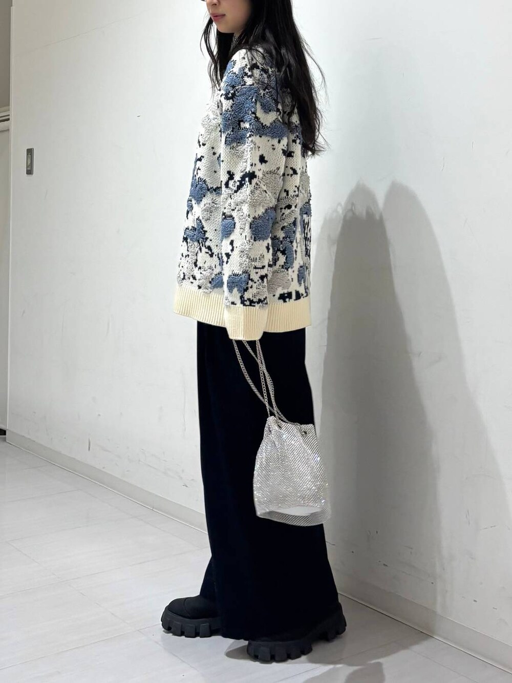 シルバー系のショルダーバッグ、ブルー系のスラックス、ホワイト系のニット/セーターを着用したレディースの冬コーディネートの2枚目の写真