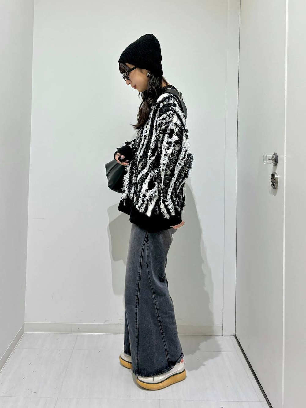 ブラック系のデニムパンツ、ブラック系のニット/セーター、ブラック系のショルダーバッグを着用したレディースの秋コーディネートの3枚目の写真