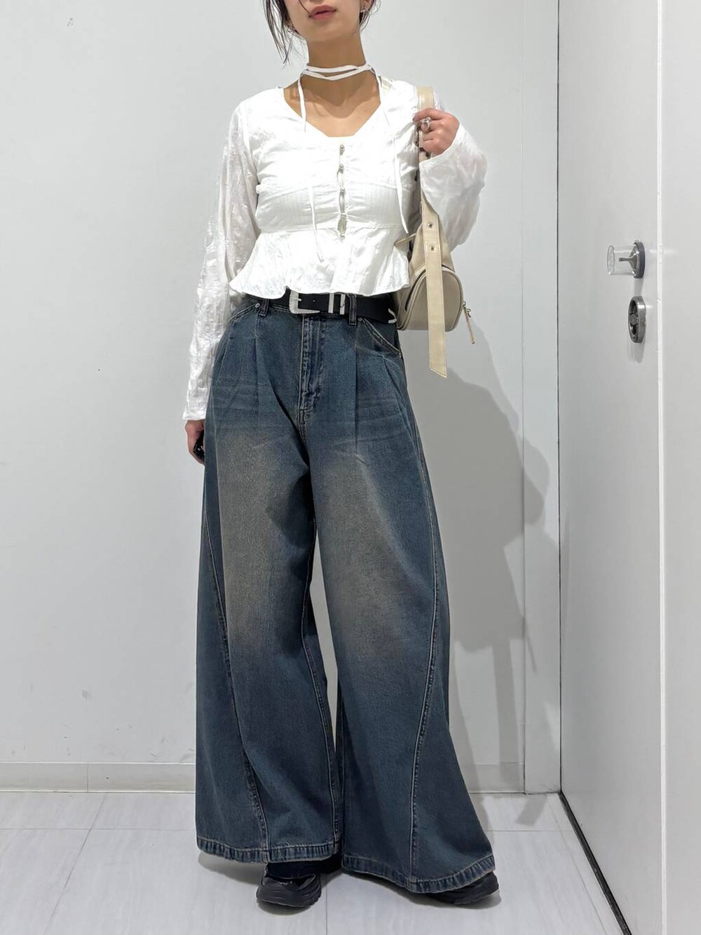 ブルー系のデニムパンツ、ブラック系のスニーカー、ホワイト系のショルダーバッグを着用したレディースの春コーディネートの6枚目の写真
