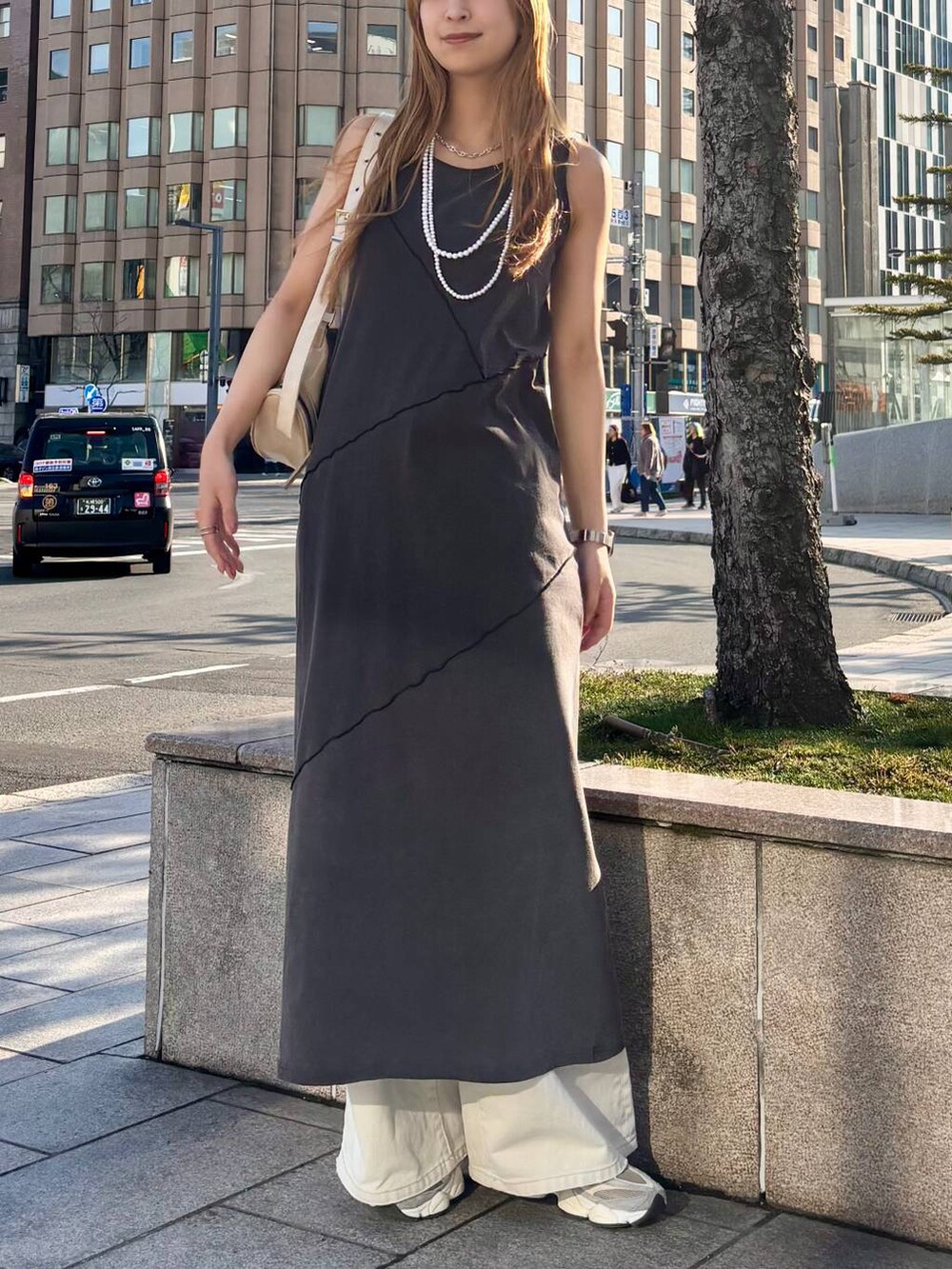 グレー系のデニムパンツ、ホワイト系のショルダーバッグ、ブラック系のワンピースを着用したレディースの春コーディネートの2枚目の写真