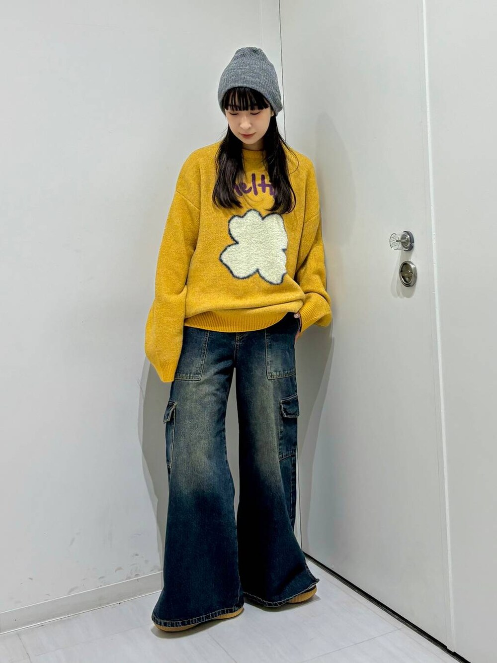 イエロー系のニット/セーター、ブルー系のデニムパンツ、グレー系のニットキャップ/ビーニーを着用したレディースの冬コーディネートの2枚目の写真