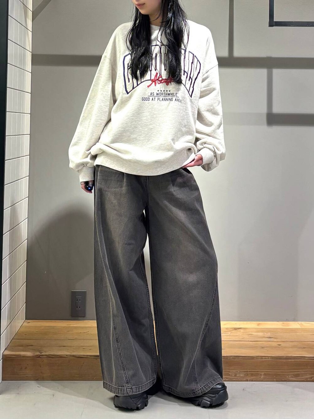 ブラック系のデニムパンツ、ベージュ系のスウェット、ブラック系のブーツを着用したレディースの秋コーディネートの2枚目の写真