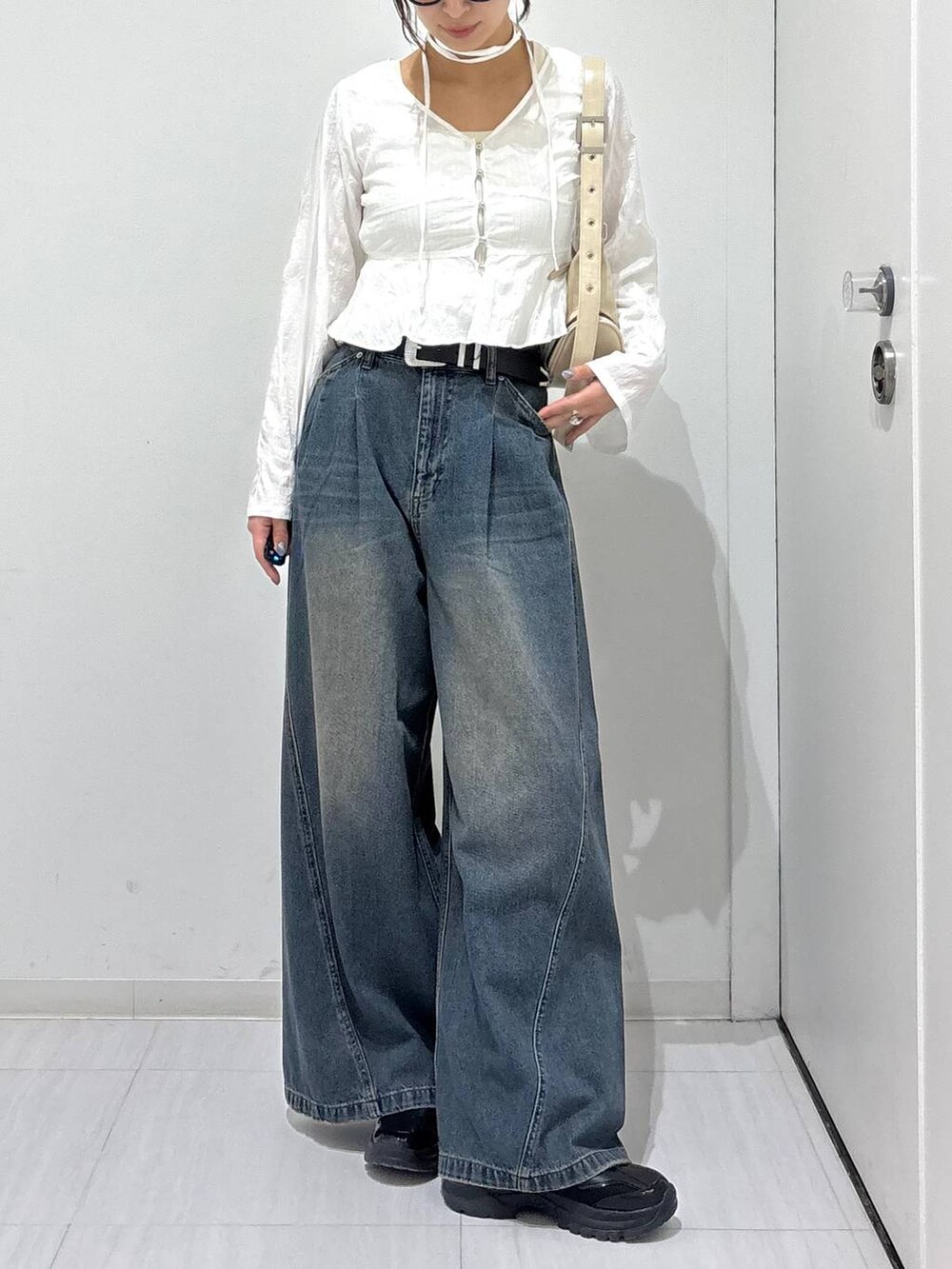 ブルー系のデニムパンツ、ブラック系のスニーカー、ホワイト系のショルダーバッグを着用したレディースの春コーディネートの2枚目の写真