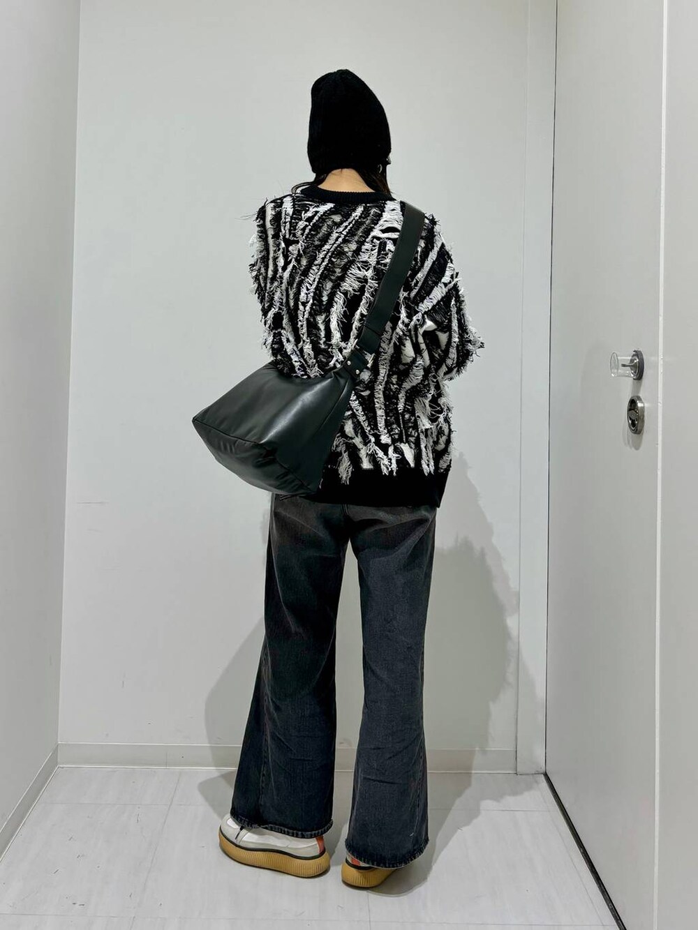 ブラック系のデニムパンツ、ブラック系のニット/セーター、ブラック系のショルダーバッグを着用したレディースの秋コーディネートの4枚目の写真