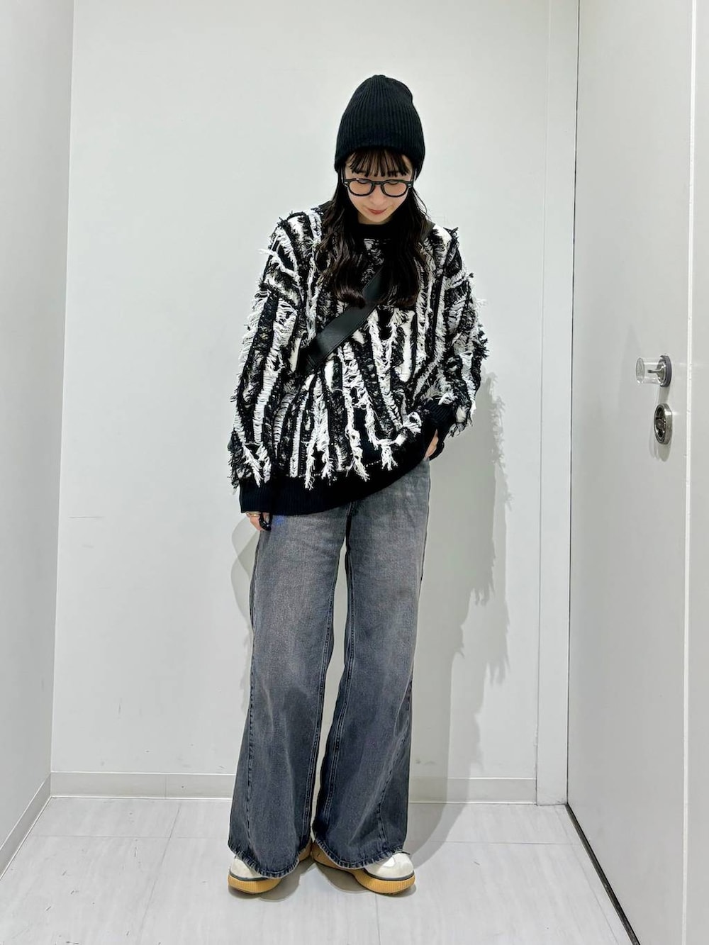 ブラック系のデニムパンツ、ブラック系のニット/セーター、ブラック系のショルダーバッグを着用したレディースの秋コーディネートの2枚目の写真