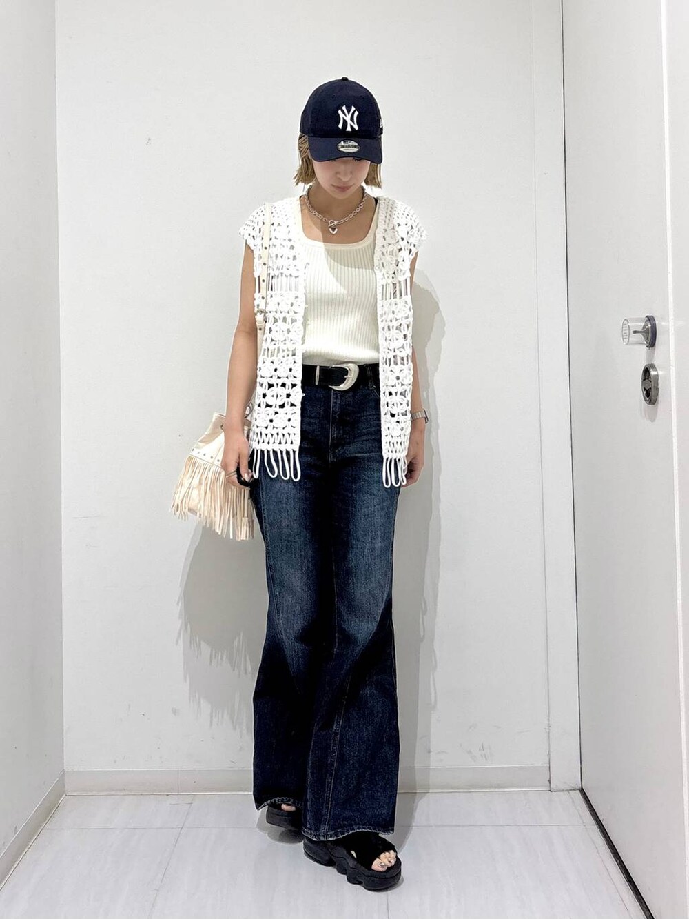 ホワイト系のタンクトップ、ブルー系のデニムパンツ、ホワイト系のベストを着用したレディースの夏コーディネートの2枚目の写真