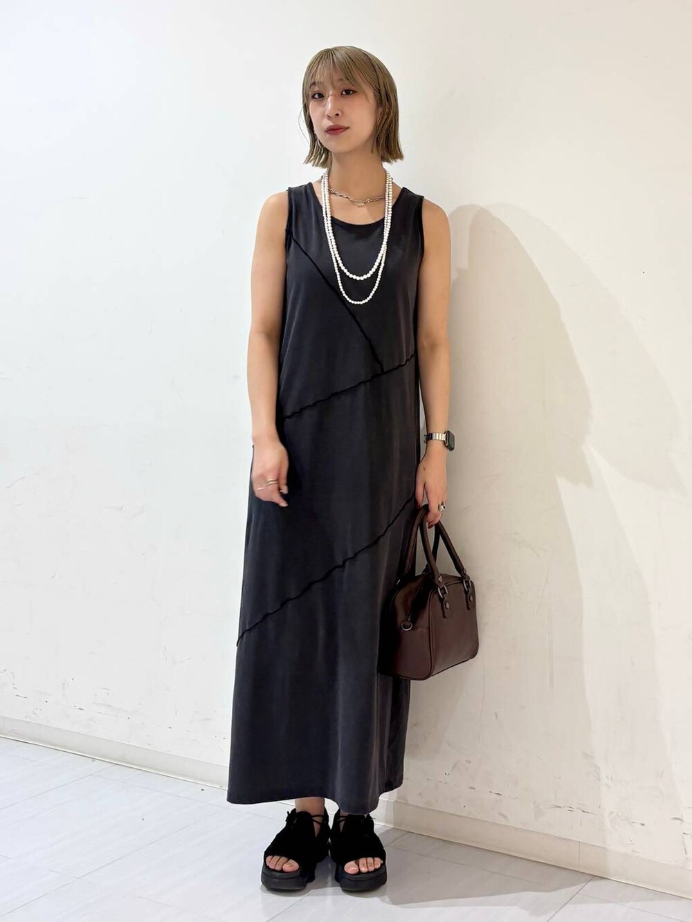 ブラック系のワンピース、ブラウン系のショルダーバッグ、ホワイト系のネックレスを着用したレディースの夏コーディネートの2枚目の写真
