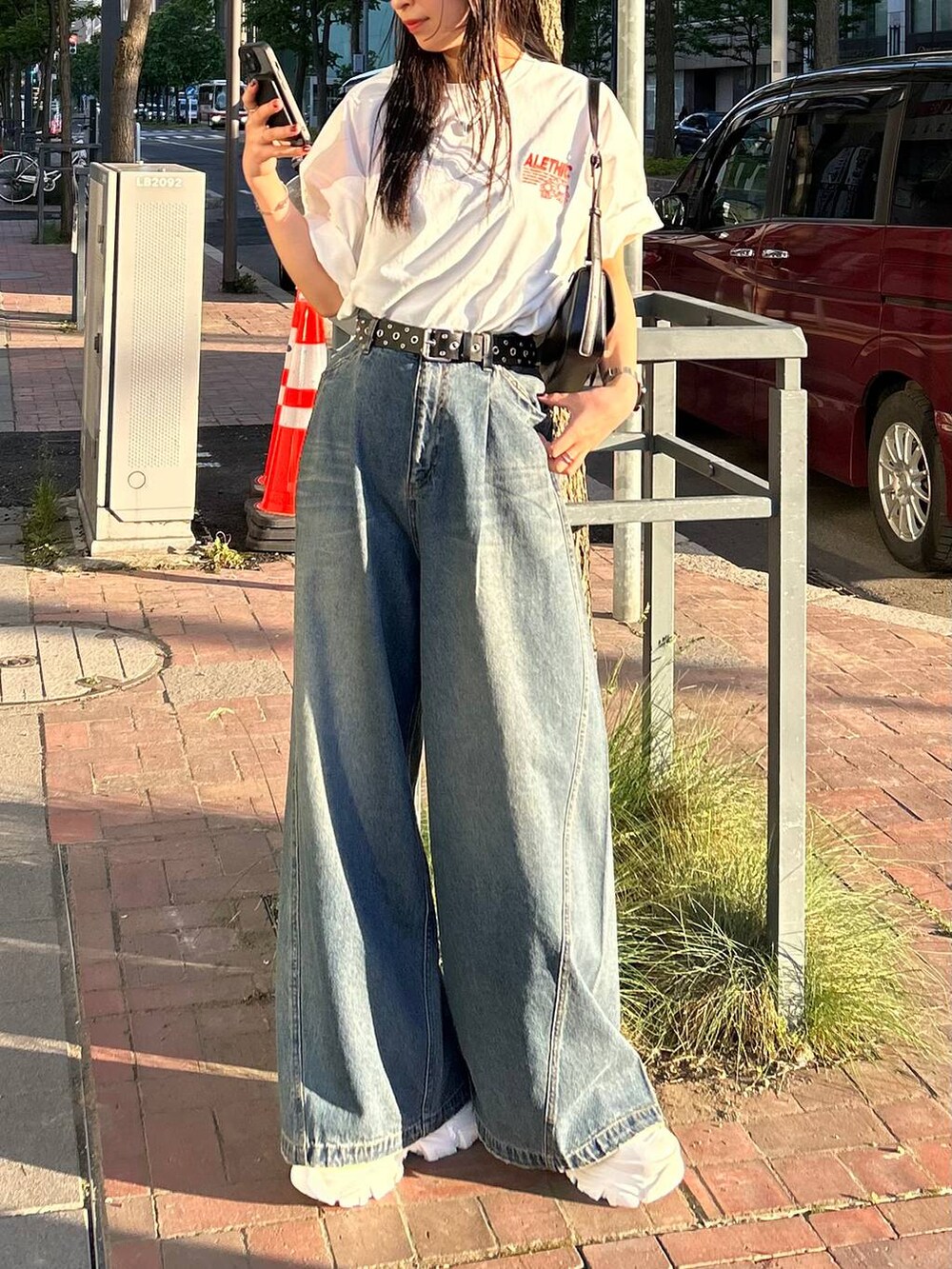 ホワイト系のスニーカー、ブラック系のハンドバッグ、ブルー系のデニムパンツを着用したレディースの夏コーディネートの4枚目の写真