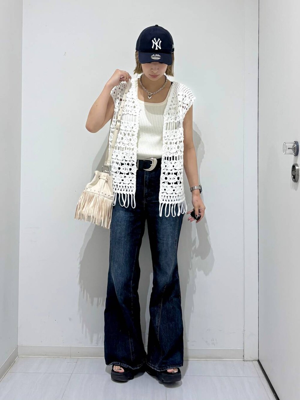 ホワイト系のタンクトップ、ブルー系のデニムパンツ、ホワイト系のベストを着用したレディースの夏コーディネートの6枚目の写真