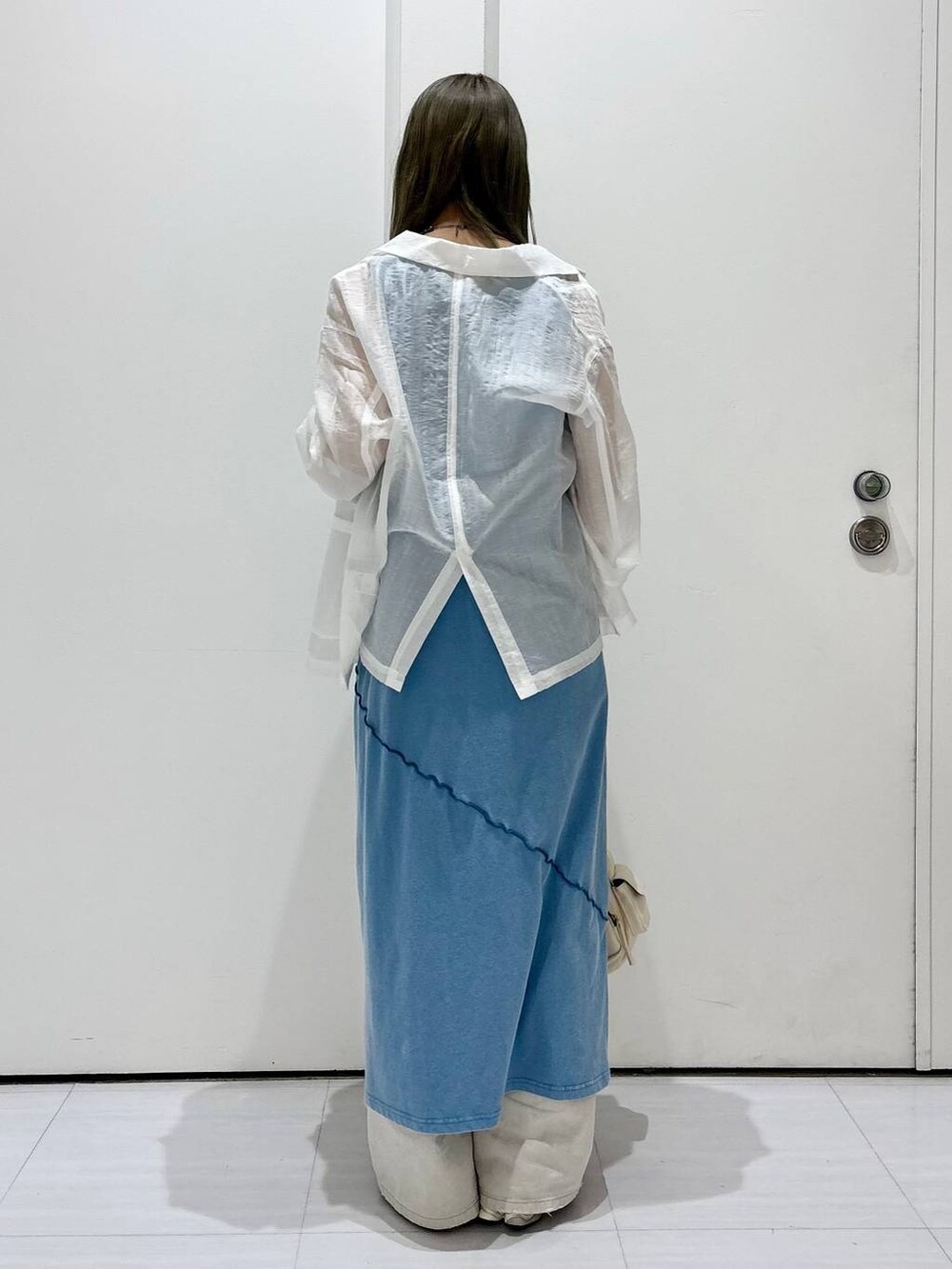 グレー系のデニムパンツ、ホワイト系のテーラードジャケット、ブルー系のワンピースを着用したレディースの春コーディネートの3枚目の写真