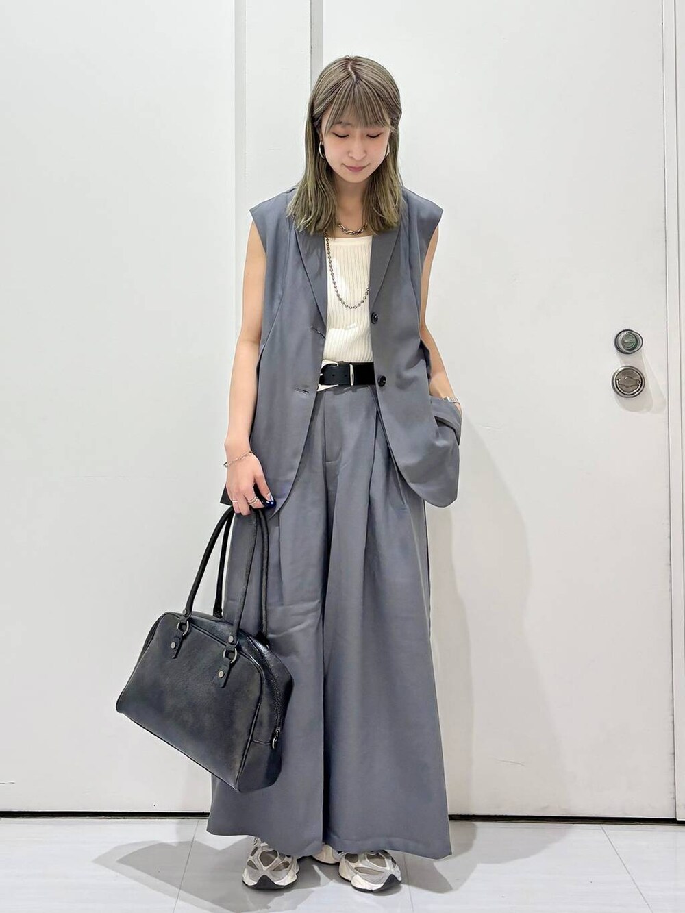 ブラック系のボストンバッグ、ホワイト系のタンクトップ、グレー系のスラックスを着用したレディースの春コーディネートの2枚目の写真
