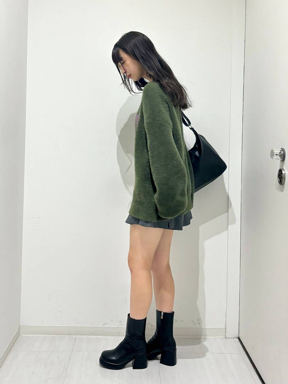 ブラック系のブーツ、グリーン系のニット/セーター、ブラック系のショルダーバッグを着用したレディースの秋コーディネートの3枚目の写真