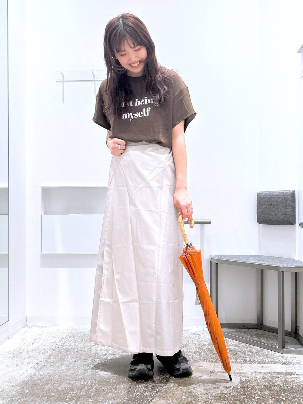 ブラウン系のスカート、ブラウン系のTシャツ/カットソー、ベージュ系のレインコート/ポンチョを着用したレディースの夏コーディネートの2枚目の写真