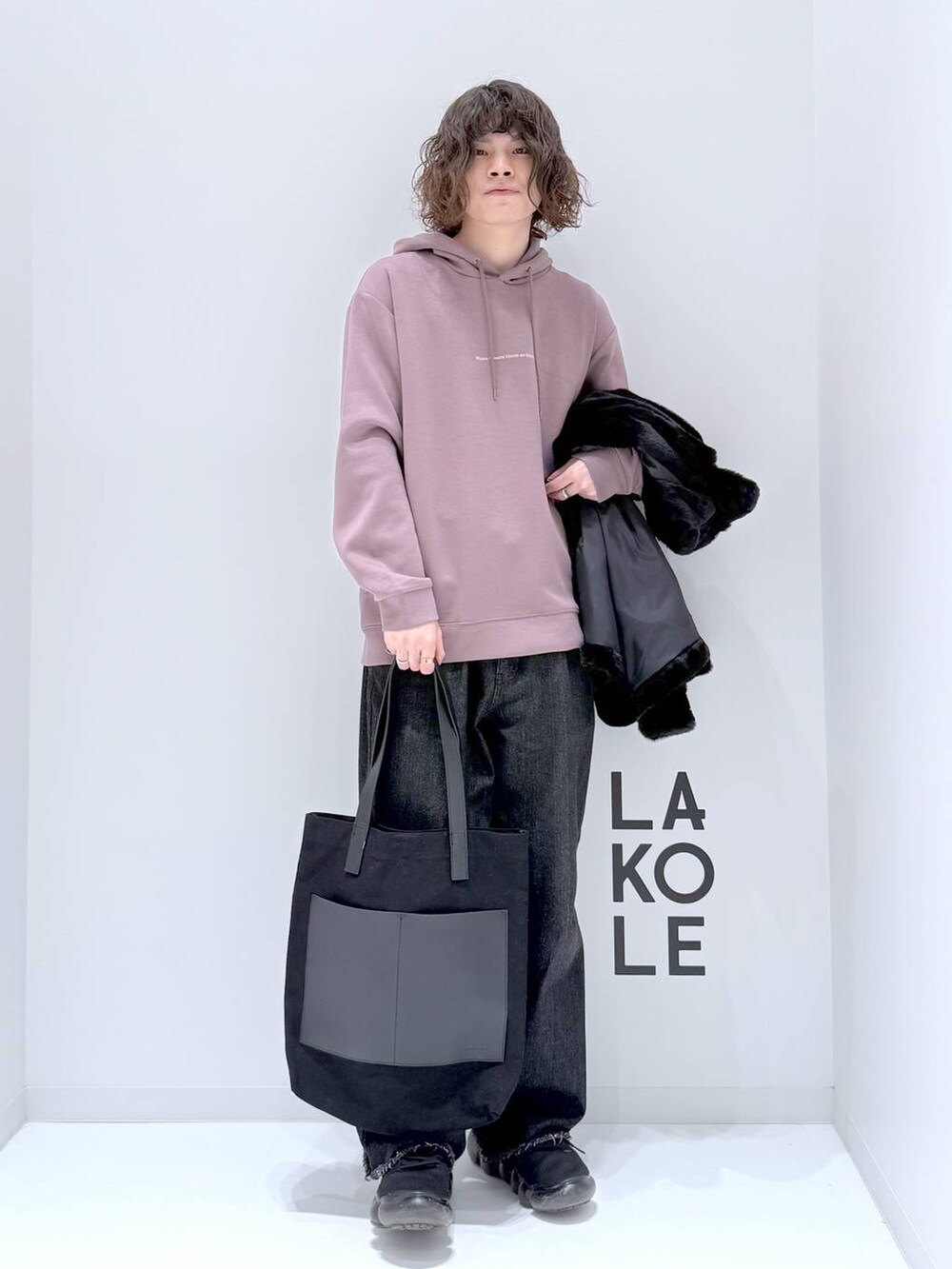 ブラック系のトートバッグ、ベージュ系のパーカー、ブラック系のデニムパンツを着用したメンズの冬コーディネートの2枚目の写真