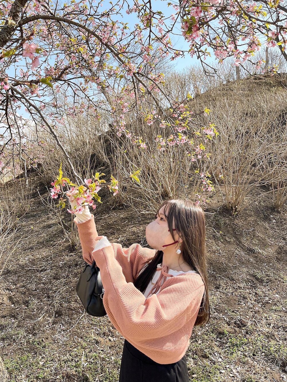 オレンジ系のカーディガン/ボレロ、ホワイト系のトップス、ブラック系のスカートを着用したレディースの春コーディネートの2枚目の写真