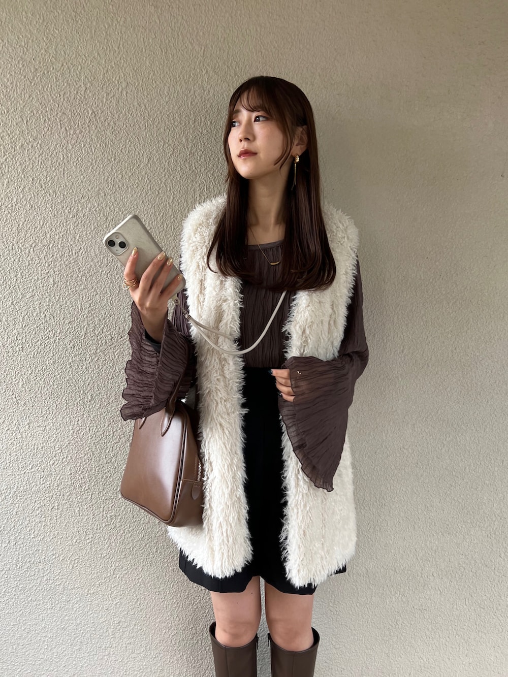 ブラウン系のトップス、ホワイト系のベスト、ブラウン系のボストンバッグを着用したレディースの秋コーディネートの2枚目の写真