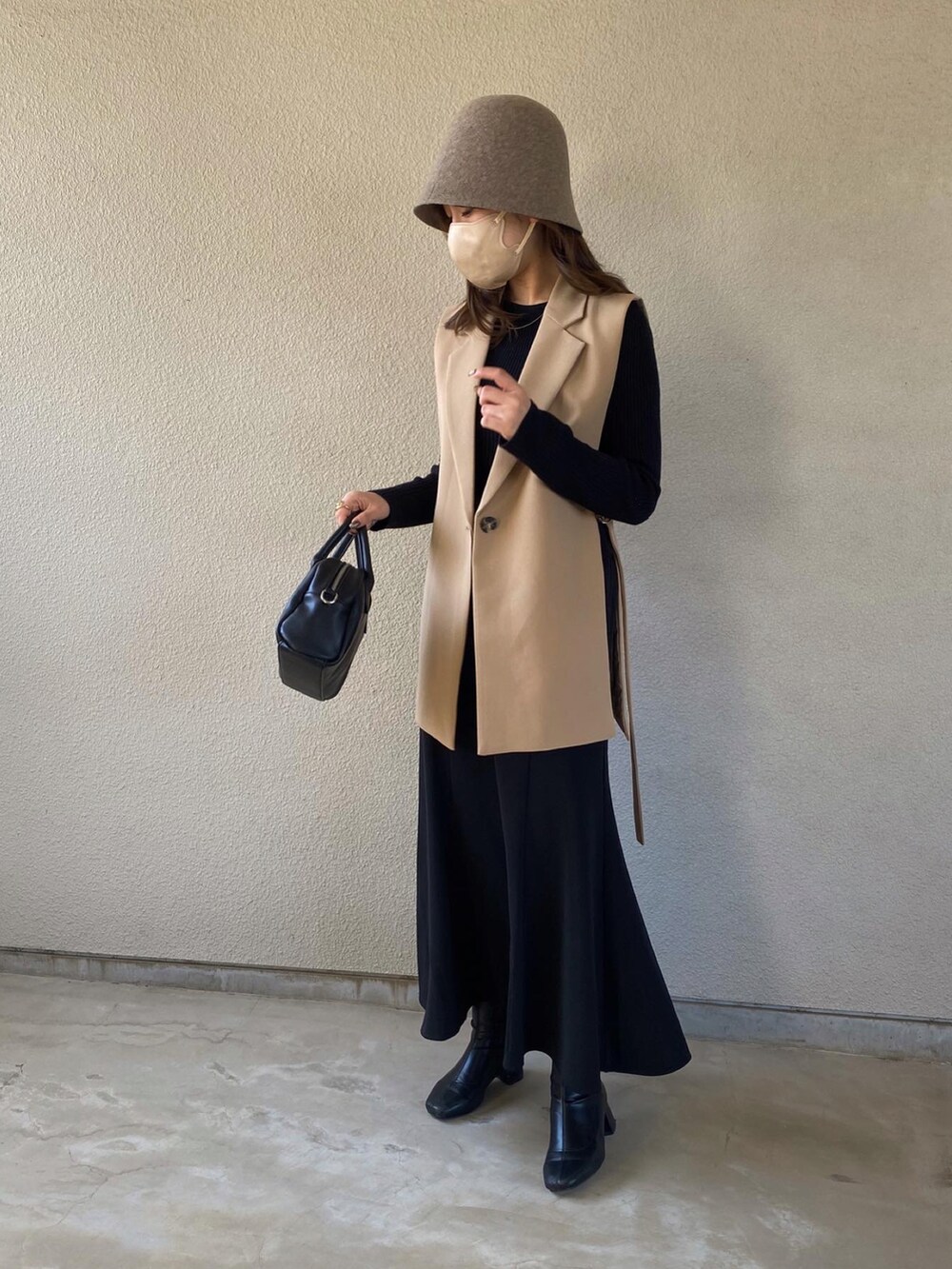 ベージュ系のベスト、ブラック系のトップス、ブラック系のスカートを着用したレディースの春コーディネートの2枚目の写真