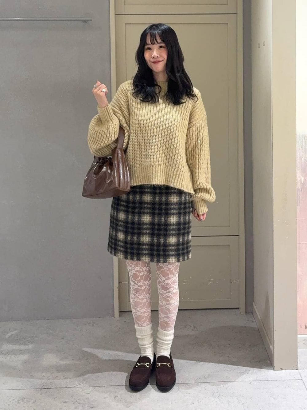 ブラウン系のローファー、ブラウン系のスカート、ベージュ系のニット/セーターを着用したレディースの冬コーディネートの2枚目の写真