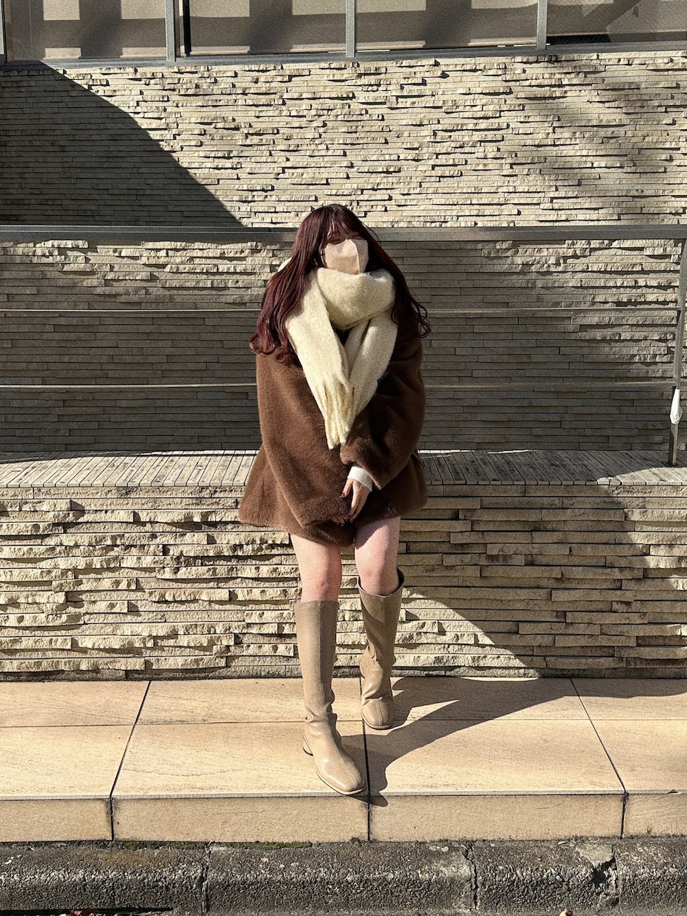 ブラウン系のノーカラーコート、ベージュ系のブーツ、ホワイト系のマフラーを着用したレディースの冬コーディネートの2枚目の写真