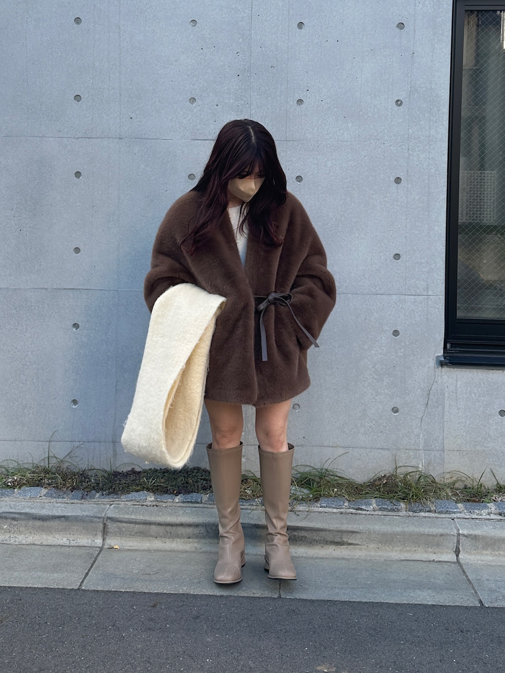 ブラウン系のノーカラーコート、ベージュ系のブーツ、ホワイト系のマフラーを着用したレディースの冬コーディネートの3枚目の写真