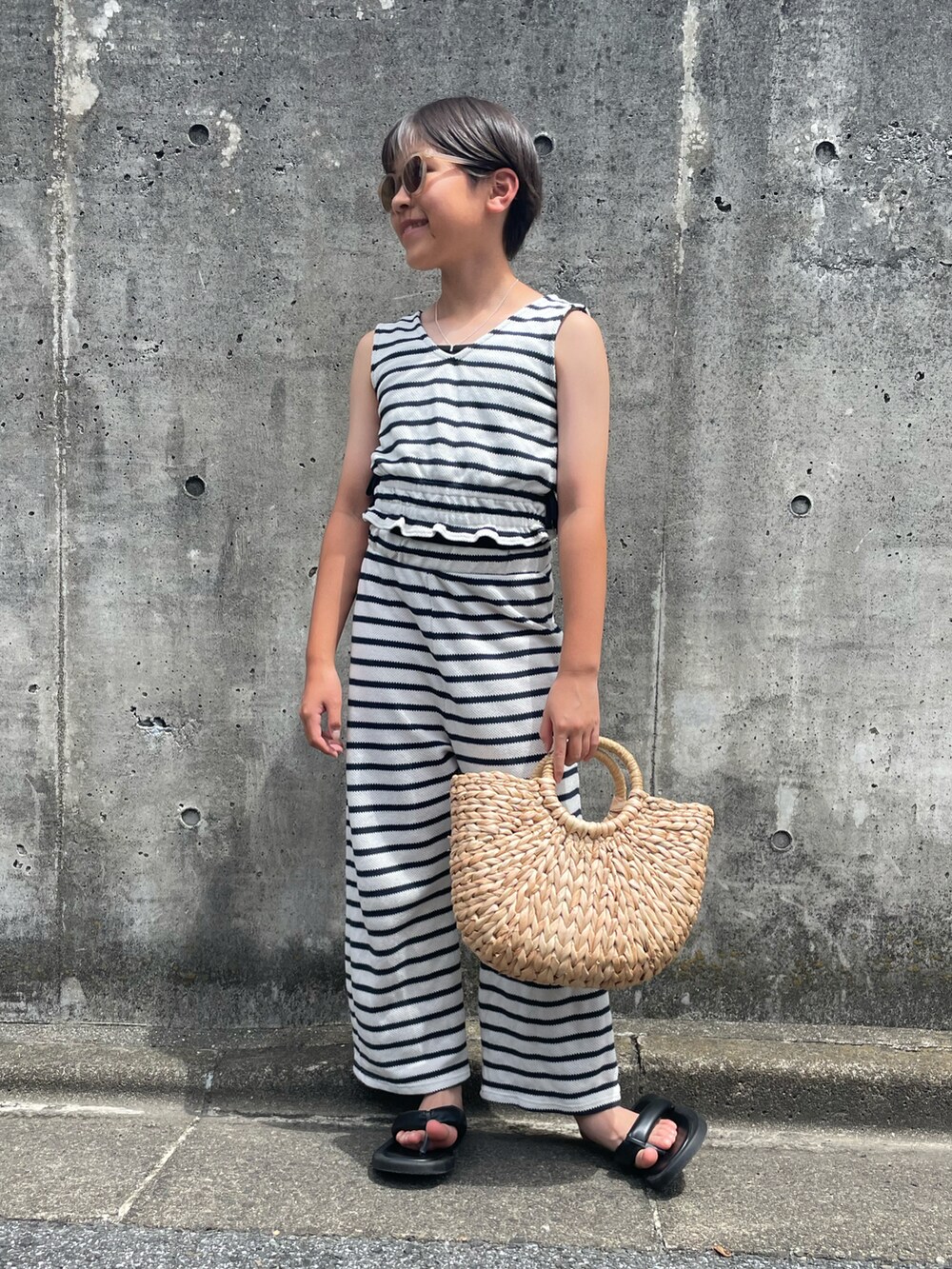 ホワイト系のアンサンブル、ベージュ系のかごバッグ、ブラック系のサンダルを着用したキッズの夏コーディネートの4枚目の写真