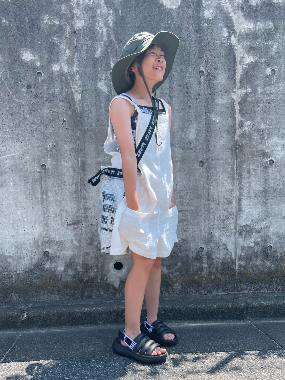 ホワイト系のサロペット/オーバーオール、ブラック系のキャミソール、ブラック系のトートバッグを着用したキッズの夏コーディネートの3枚目の写真