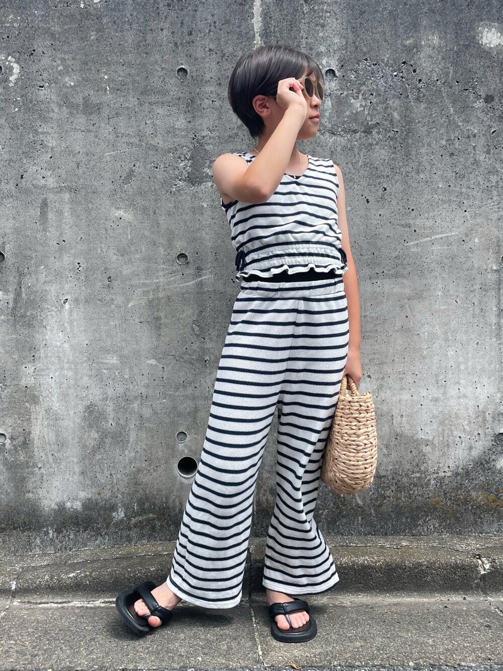 ホワイト系のアンサンブル、ベージュ系のかごバッグ、ブラック系のサンダルを着用したキッズの夏コーディネートの5枚目の写真