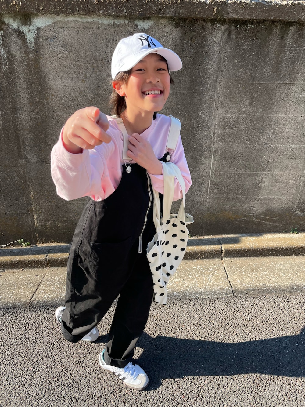 ブラック系のサロペット/オーバーオール、ピンク系のTシャツ/カットソー、ホワイト系のトートバッグを着用したキッズの春コーディネートの2枚目の写真