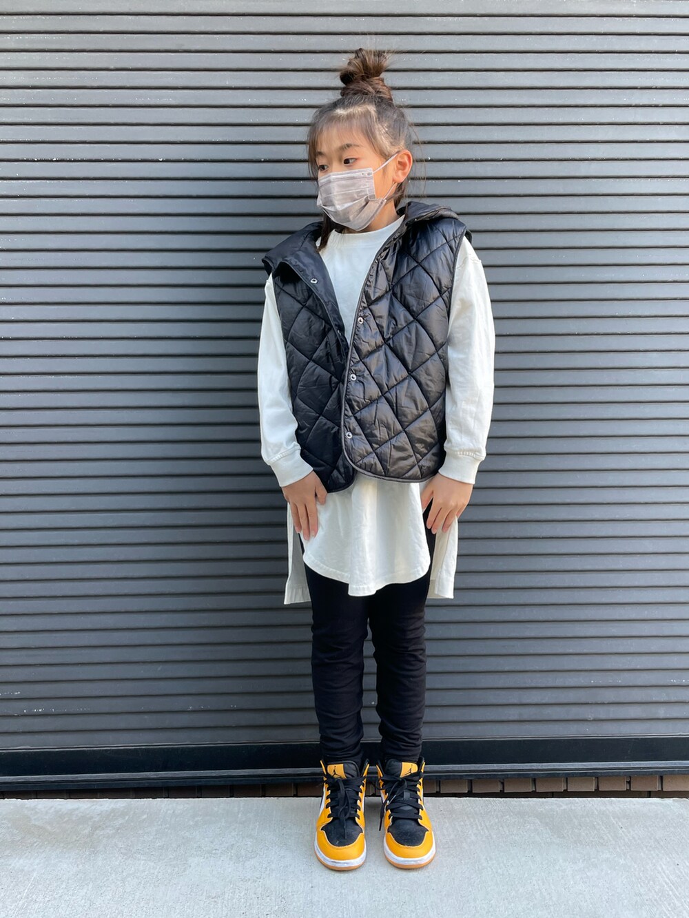 ブラック系のダウンベスト、ホワイト系のTシャツ/カットソー、オレンジ系のスニーカーを着用したキッズの春コーディネートの2枚目の写真