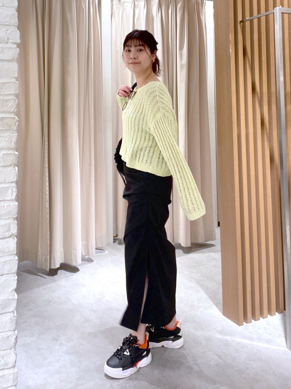 イエロー系のニット/セーター、ブラック系のスカート、ブラック系のショルダーバッグを着用したレディースの春コーディネートの3枚目の写真