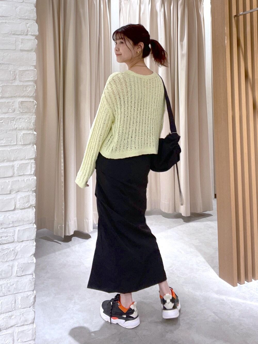イエロー系のニット/セーター、ブラック系のスカート、ブラック系のショルダーバッグを着用したレディースの春コーディネートの4枚目の写真