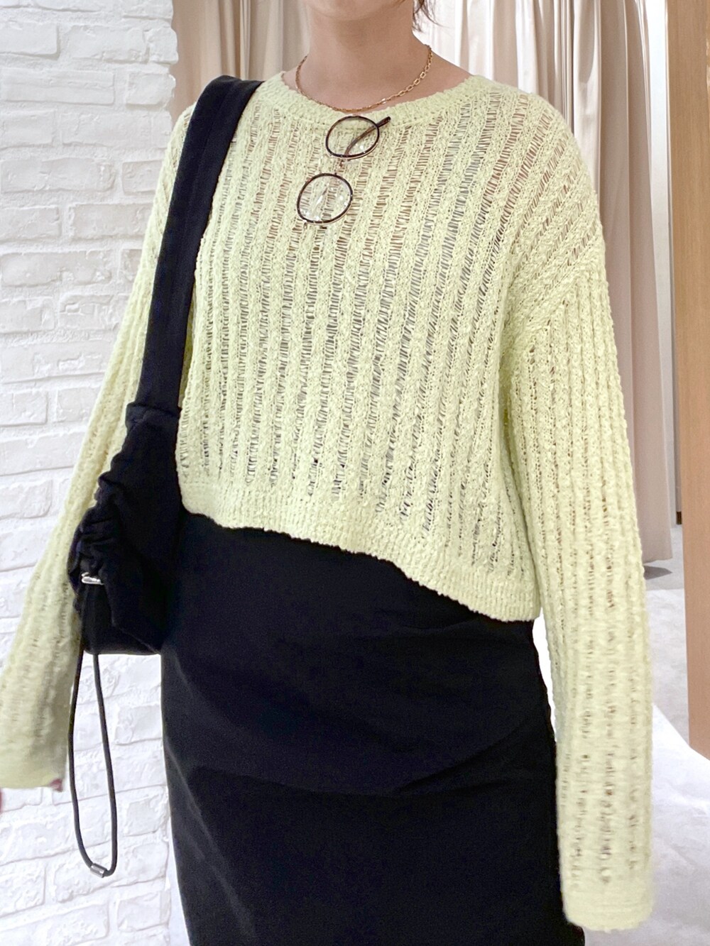 イエロー系のニット/セーター、ブラック系のスカート、ブラック系のショルダーバッグを着用したレディースの春コーディネートの5枚目の写真