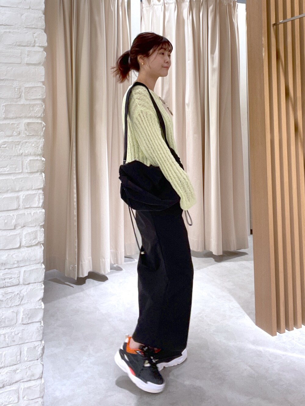 イエロー系のニット/セーター、ブラック系のスカート、ブラック系のショルダーバッグを着用したレディースの春コーディネートの2枚目の写真