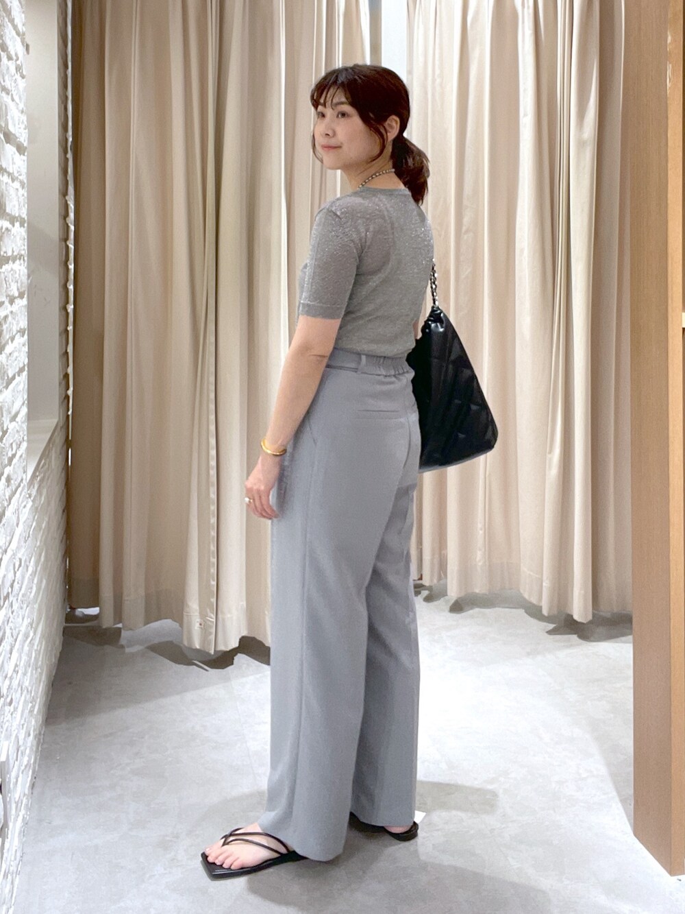 シルバー系のニット/セーター、グレー系のスラックス、ブラック系のサンダルを着用したレディースの夏コーディネートの3枚目の写真