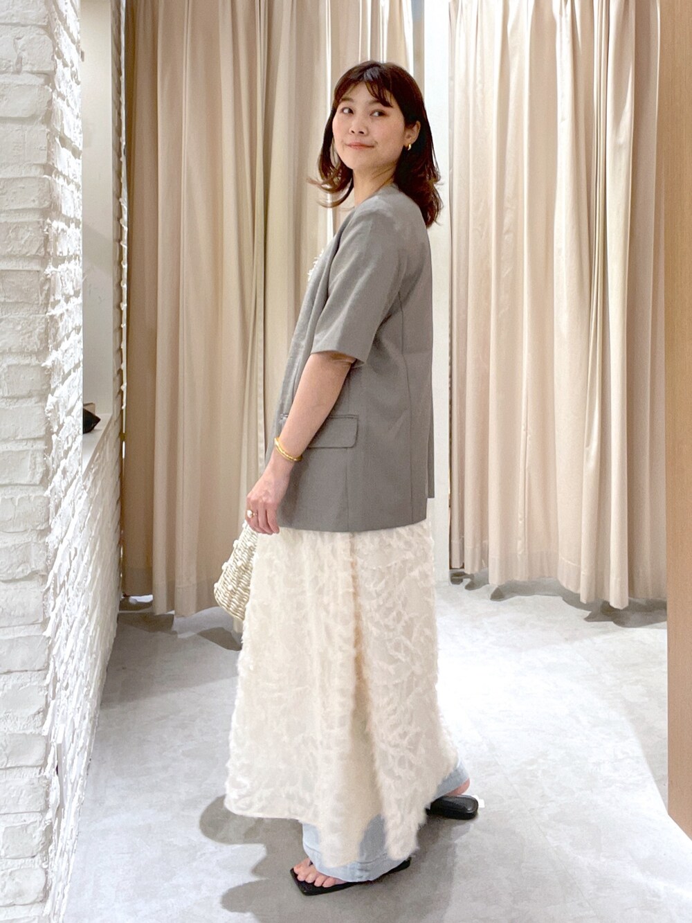 グレー系のノーカラージャケット、ホワイト系のワンピース、ブラック系のサンダルを着用したレディースの夏コーディネートの2枚目の写真