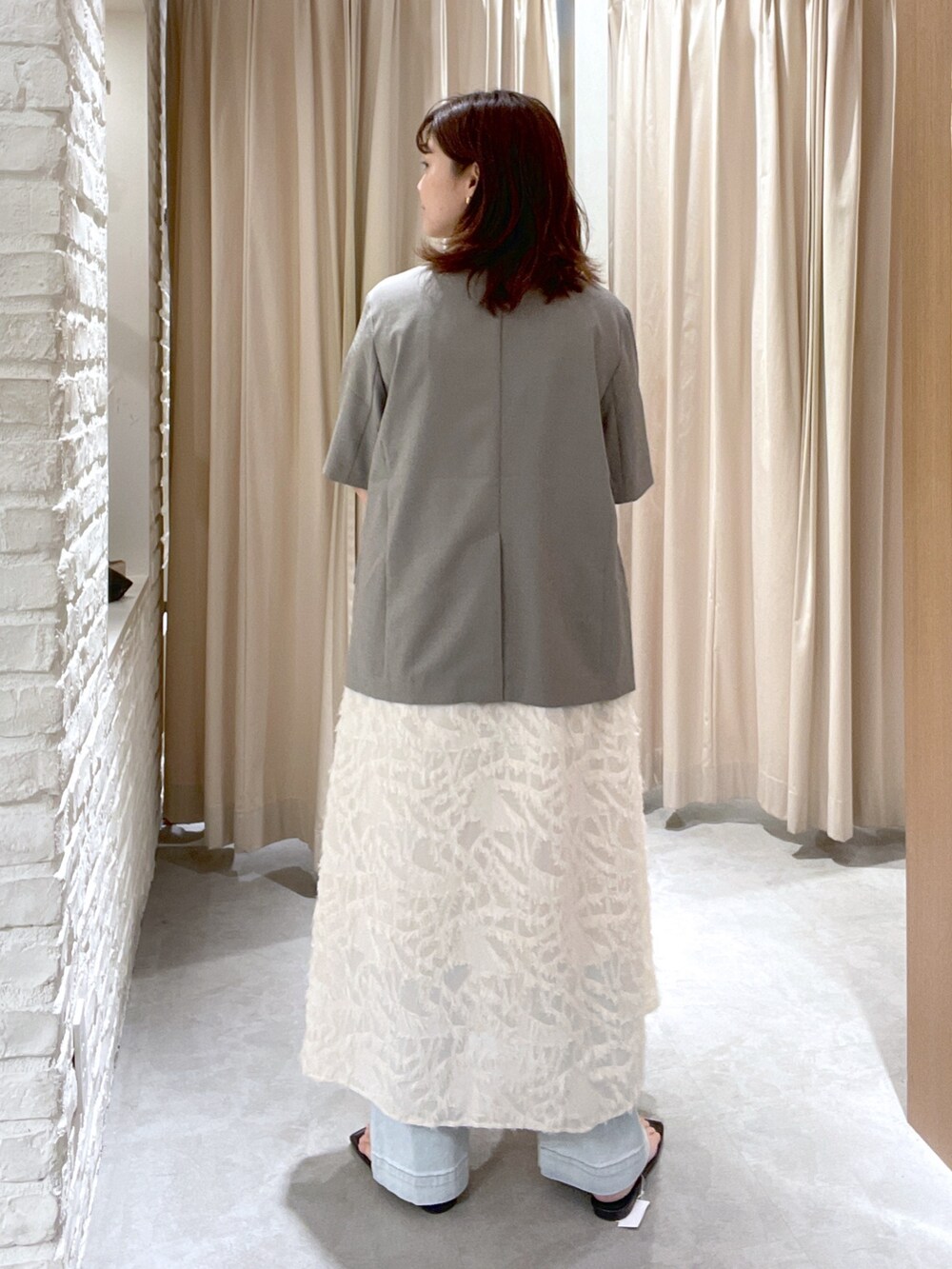 グレー系のノーカラージャケット、ホワイト系のワンピース、ブラック系のサンダルを着用したレディースの夏コーディネートの3枚目の写真