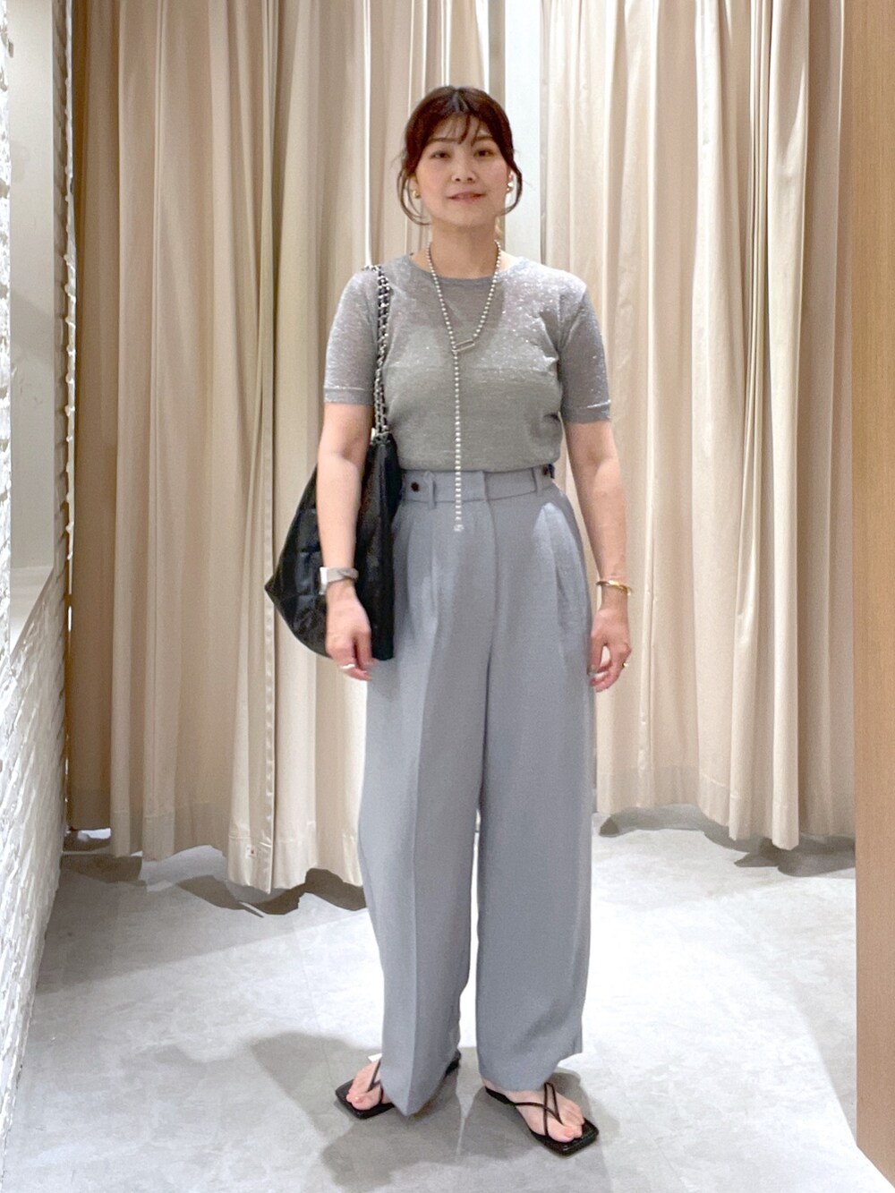 シルバー系のニット/セーター、グレー系のスラックス、ブラック系のサンダルを着用したレディースの夏コーディネートの2枚目の写真