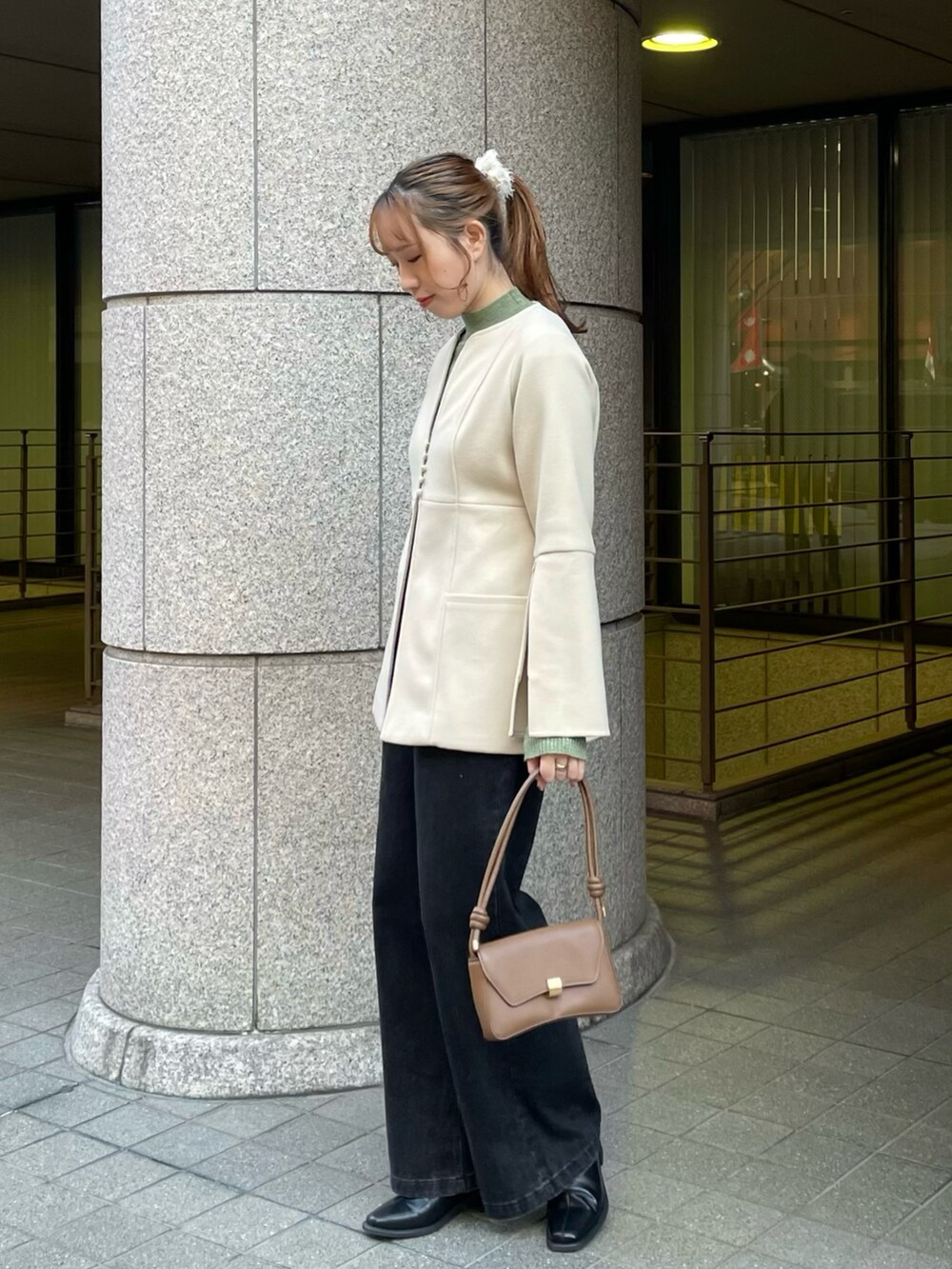 ホワイト系のノーカラーコート、グリーン系のニット/セーター、ブラック系のデニムパンツを着用したレディースの冬コーディネートの3枚目の写真