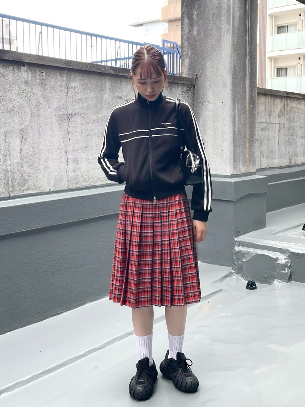 ブラック系のスニーカー、レッド系のスカート、ブラック系のショルダーバッグを着用したレディースの秋コーディネートの3枚目の写真