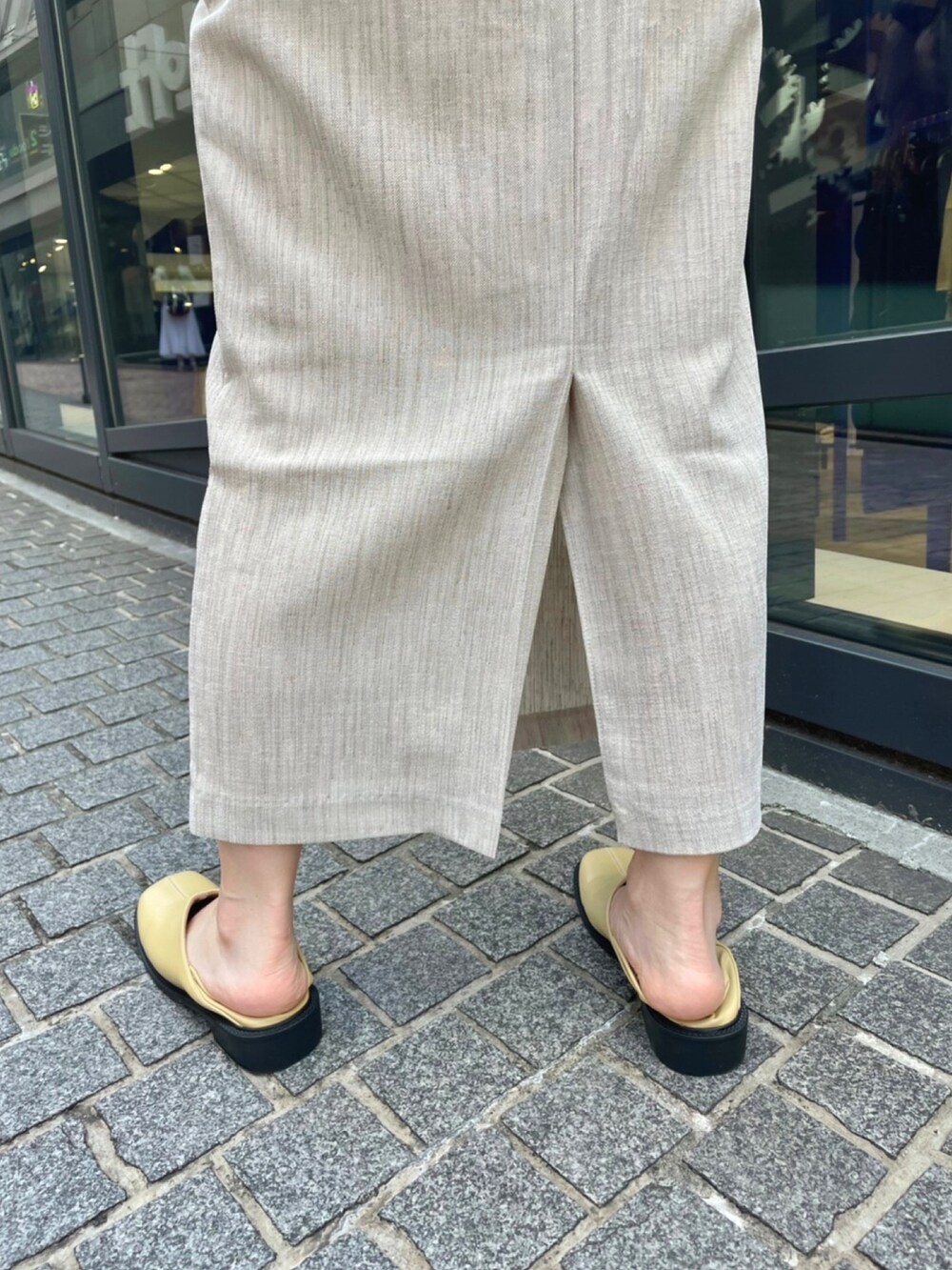 イエロー系のベスト、ベージュ系のスカート、ベージュ系のローファーを着用したレディースの夏コーディネートの2枚目の写真