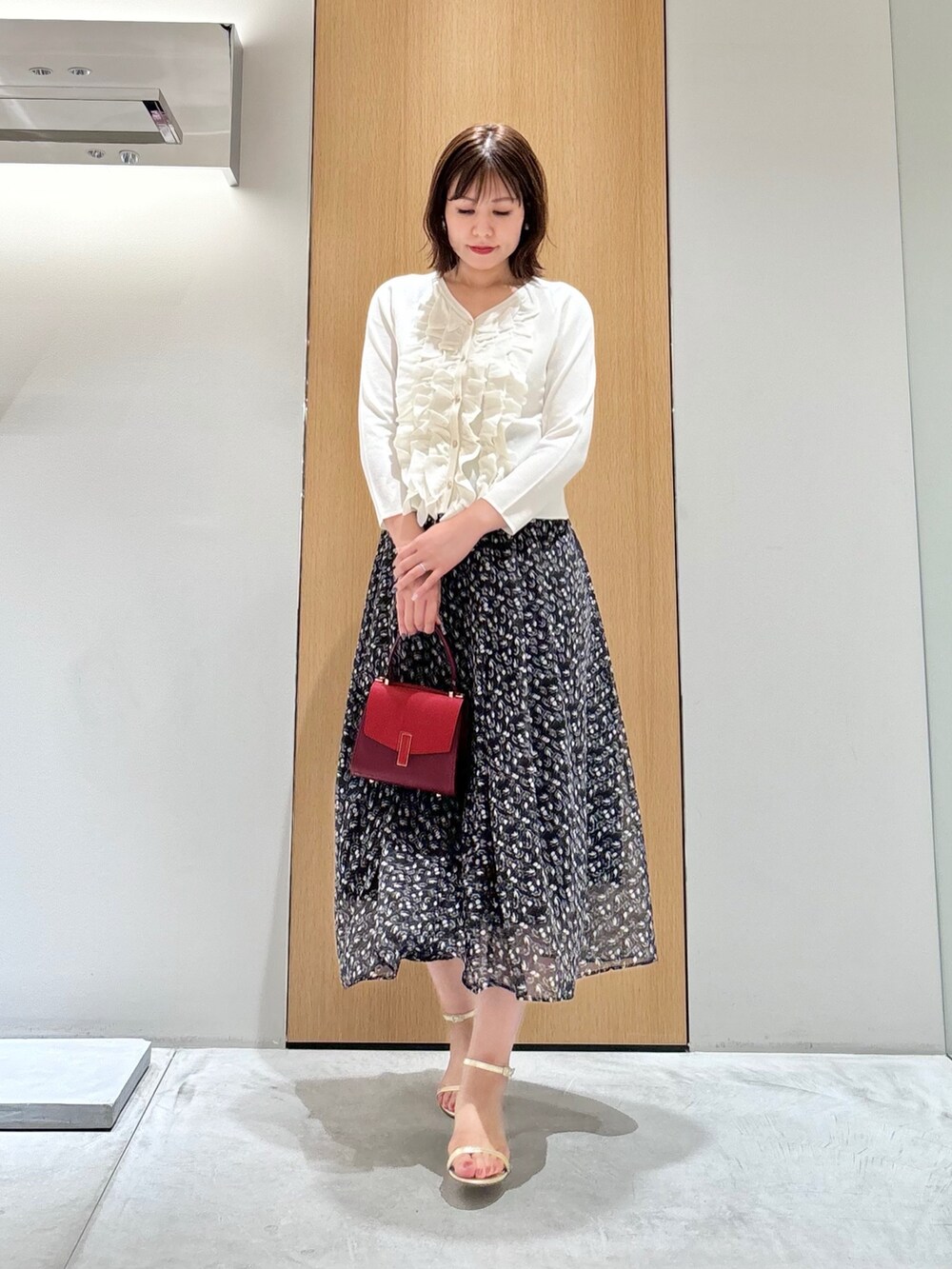 ブラック系のスカート、レッド系のハンドバッグ、ホワイト系のニット/セーターを着用したレディースの秋コーディネートの2枚目の写真