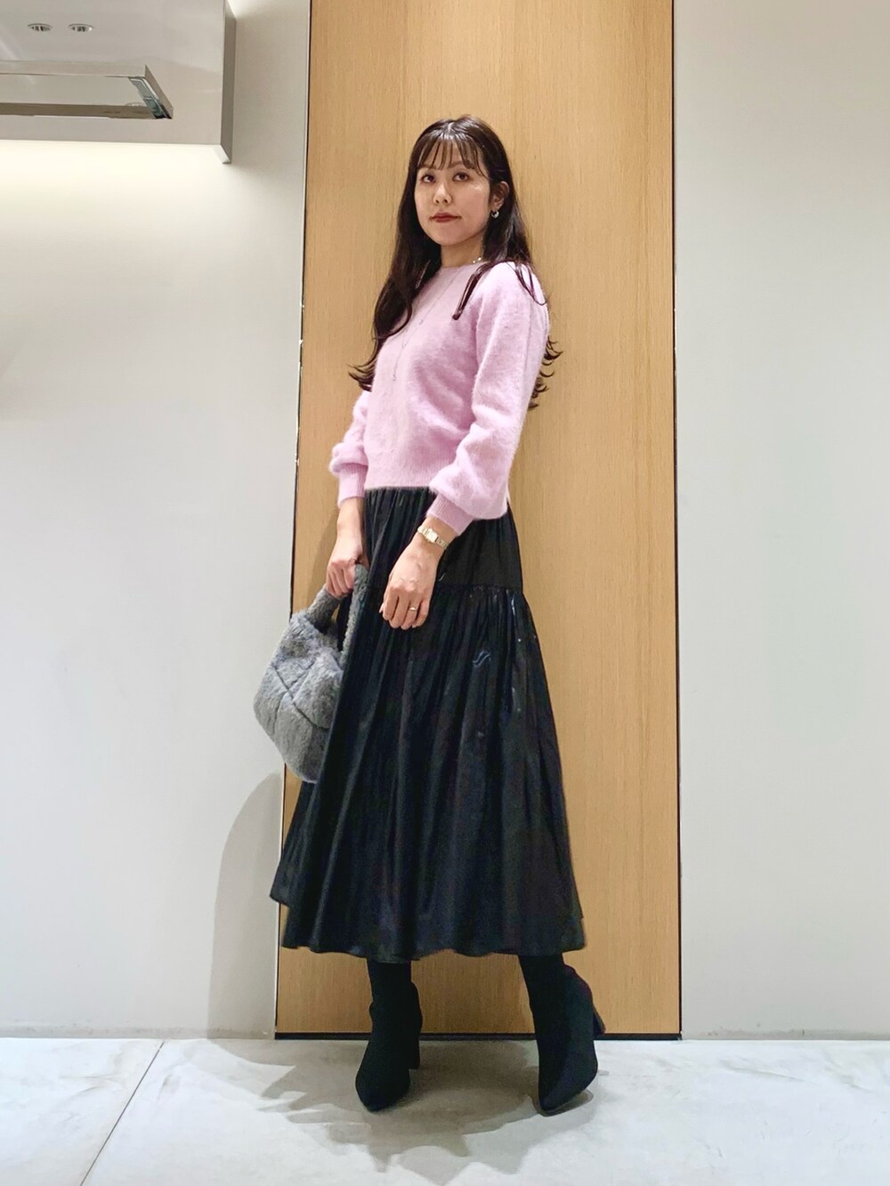 グレー系のハンドバッグ、ブラック系のスカート、パープル系のニット/セーターを着用したレディースの冬コーディネートの2枚目の写真