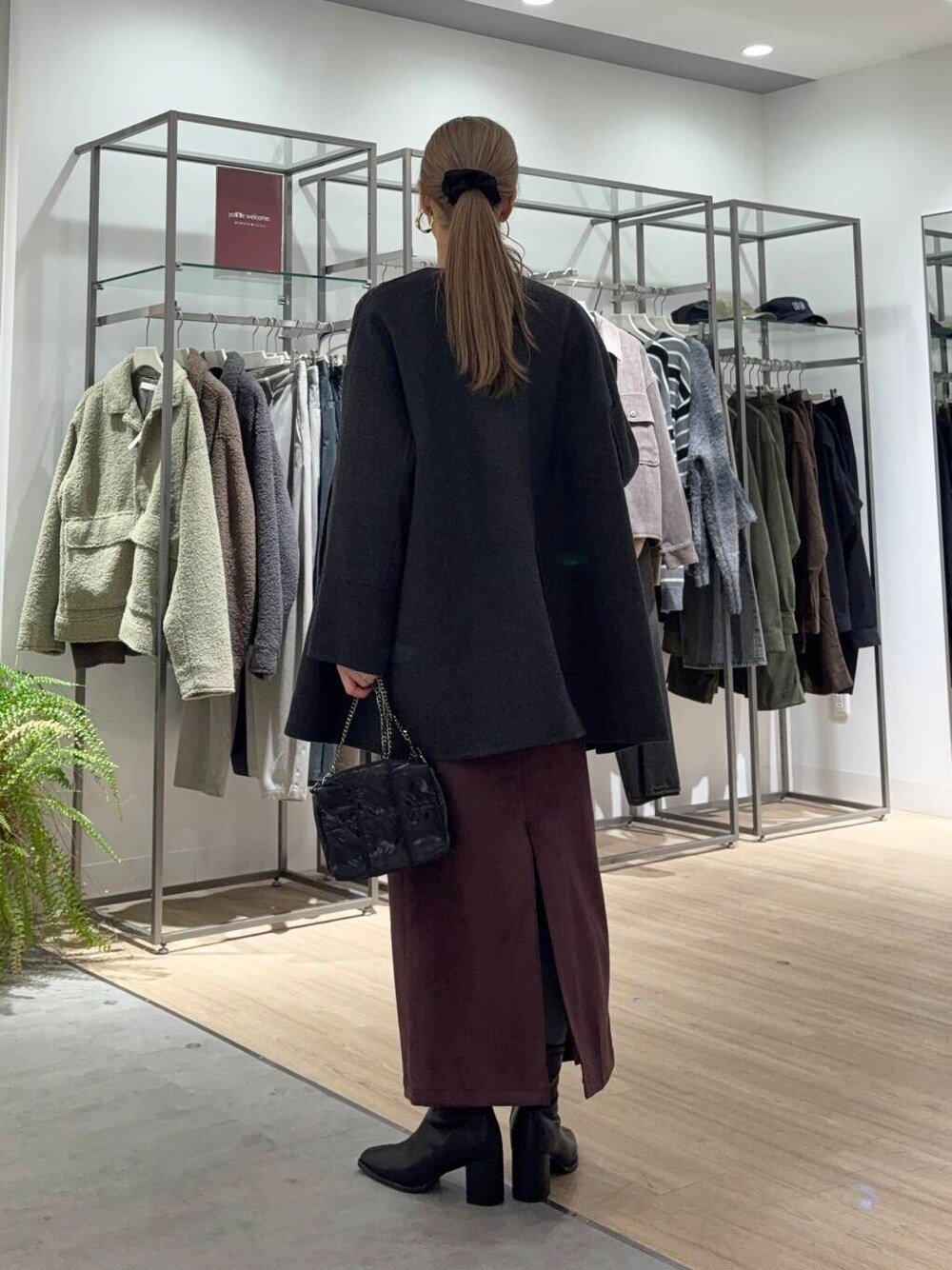 グレー系のノーカラーコート、ブラック系のブーツ、ブラック系のニット/セーターを着用したレディースの冬コーディネートの2枚目の写真