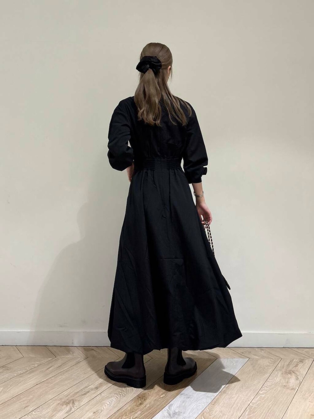 ブラック系のショルダーバッグ、ブラウン系のブーツ、ブラック系のワンピースを着用したレディースの秋コーディネートの3枚目の写真