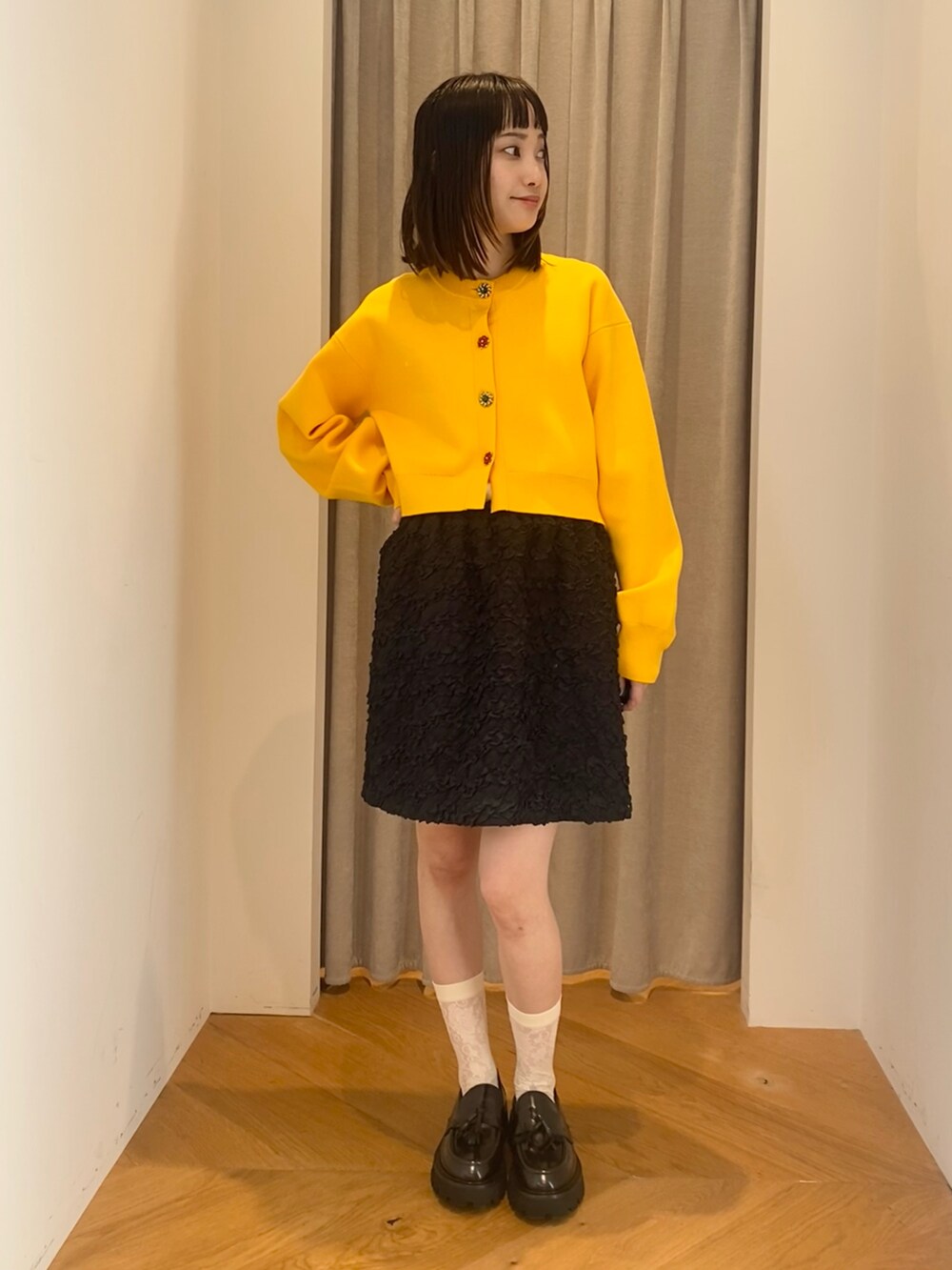 ブルー系のステンカラーコート、ブラック系のボストンバッグ、イエロー系のカーディガン/ボレロを着用したレディースの秋コーディネートの2枚目の写真