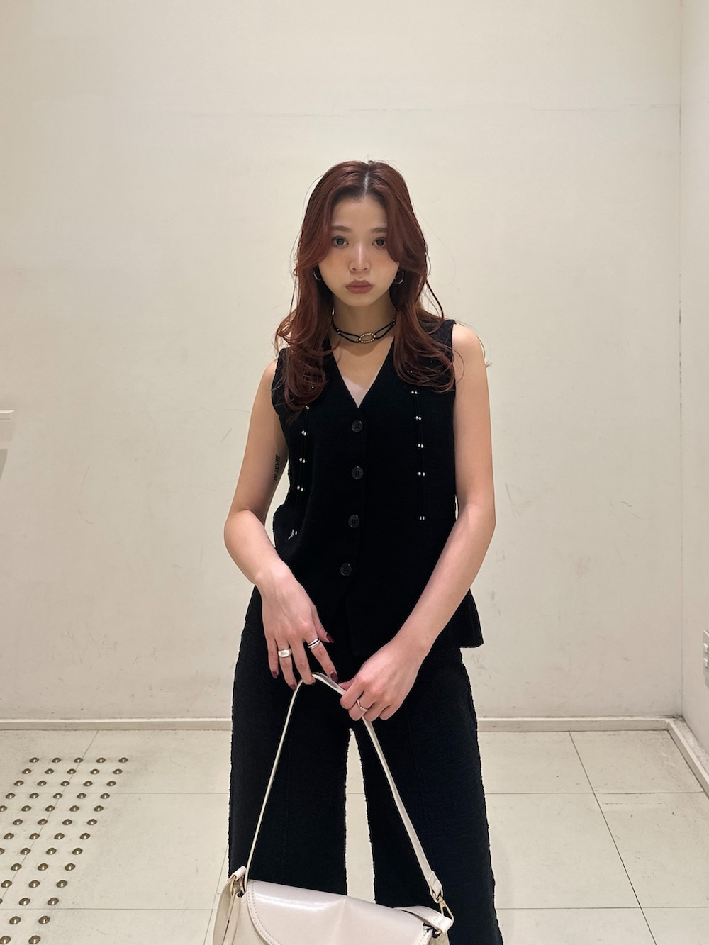 ホワイト系のショルダーバッグ、ブラック系のベスト、ブラック系のスラックスを着用したレディースの春コーディネートの2枚目の写真