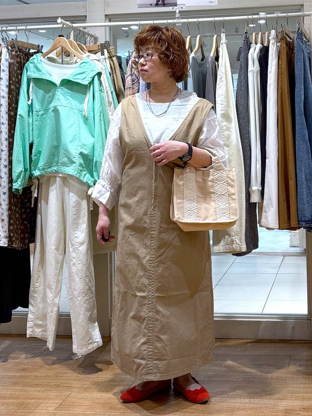 ベージュ系のジャンパースカート、ホワイト系のシャツ/ブラウス、グリーン系のタンクトップを着用したレディースの春コーディネートの2枚目の写真